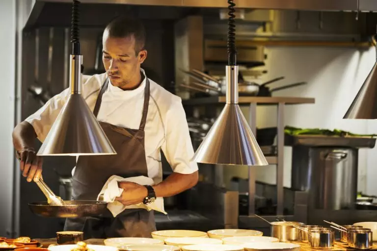 Chef standing in a restaurant kitchen, plating food.