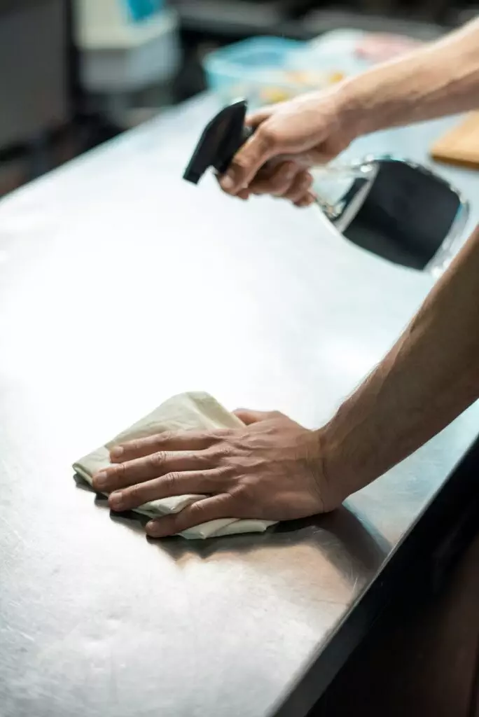 Hands of contemporary chef of restaurant spraying sanitizer on kitchen table